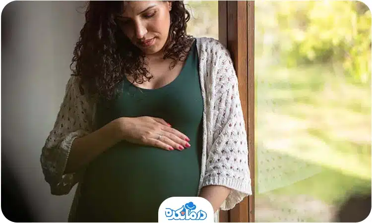  یک زن باردار که کنار پنجره ایستاده است