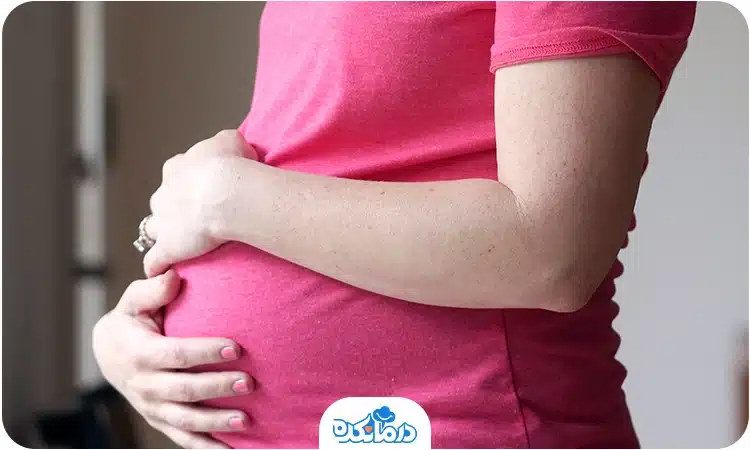 یک زن باردار که دست‌هایش را روی شکم گذاشته است